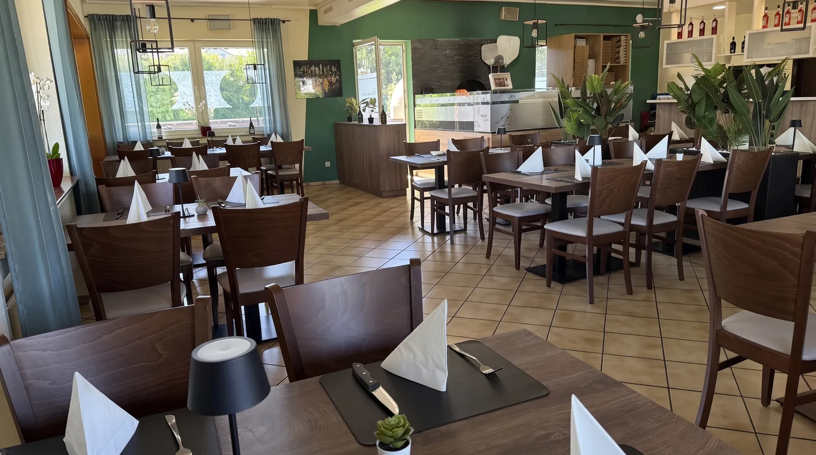 Gastraum mit gedeckten Tischen, grüner Wand, Bar und Pizzaofen