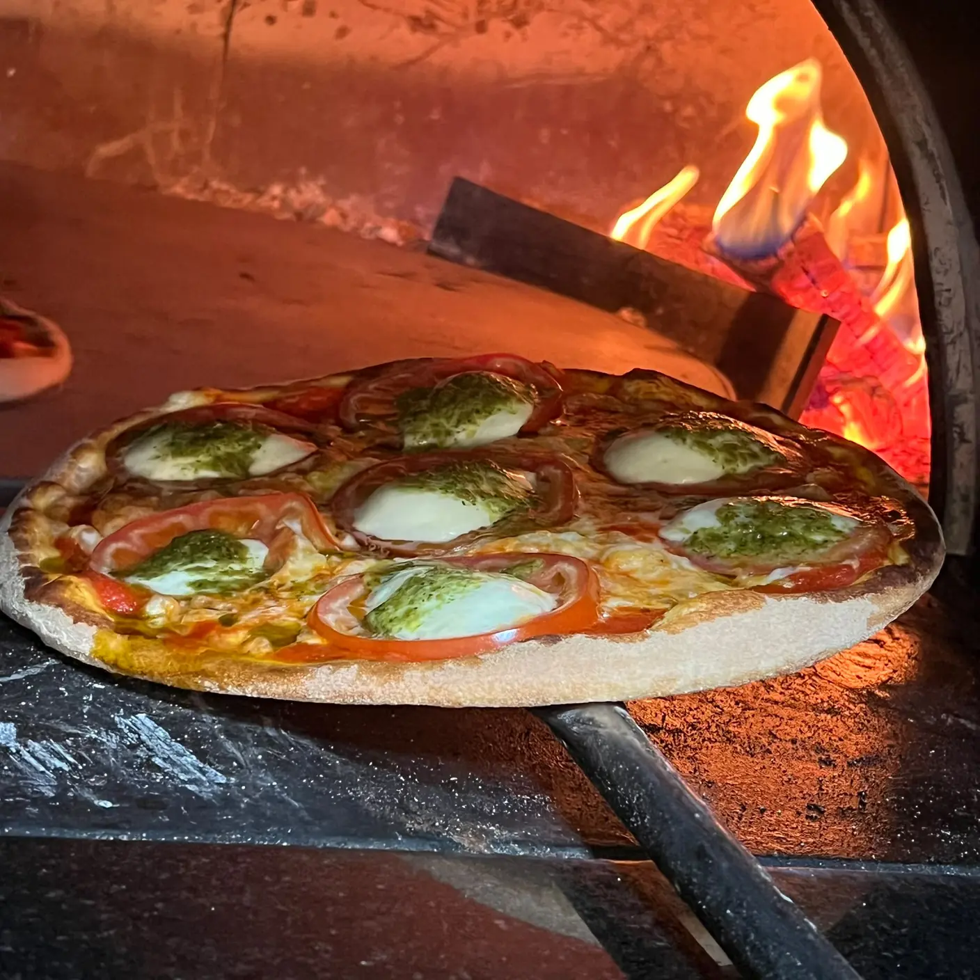 Frische Pizza mit Mozzarella, Tomaten und Pesto im heißen Holzofen
