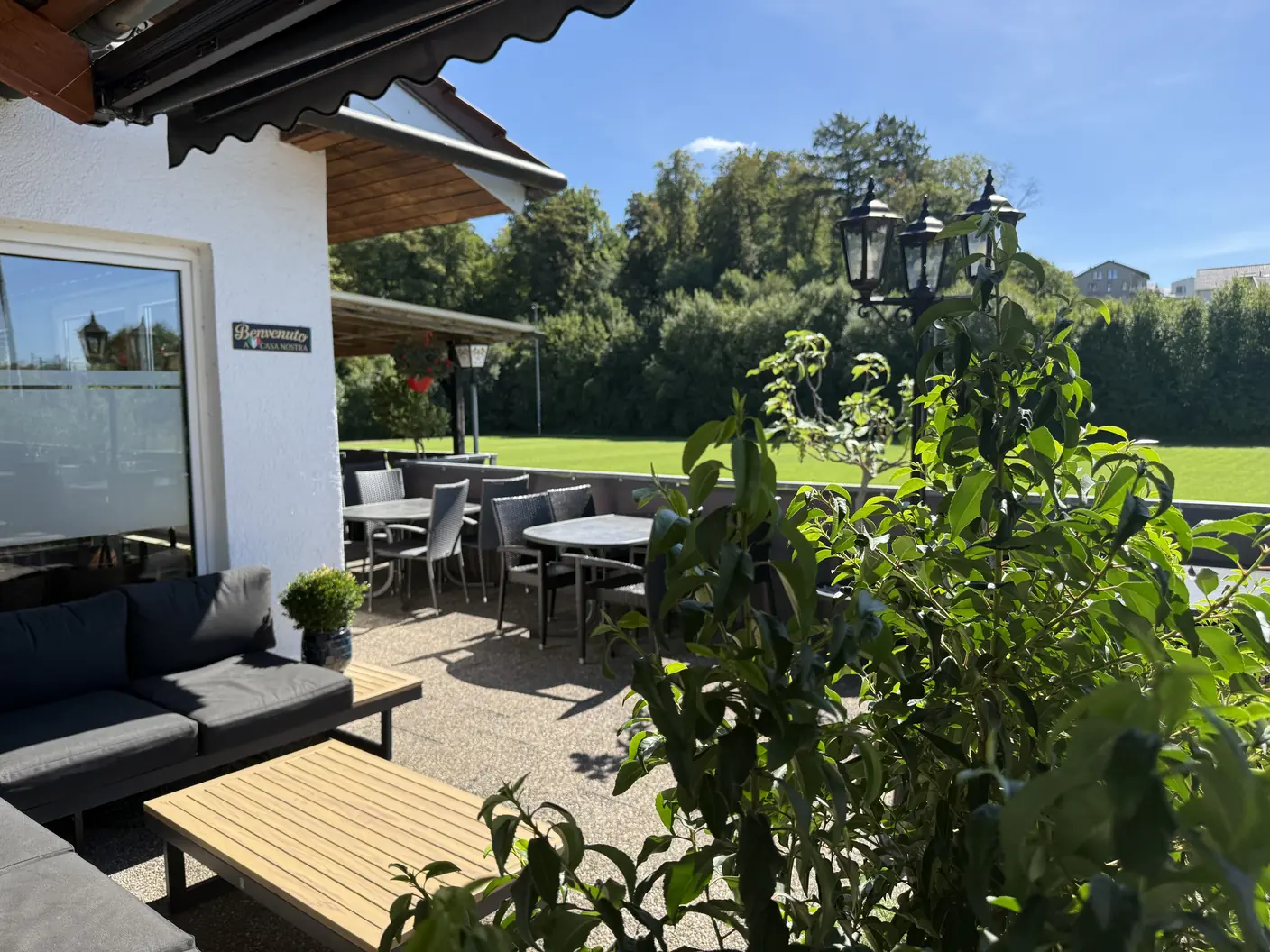 Sonnige Außenterrasse mit Lounge-Bereich, Tischen und Blick auf das Grün